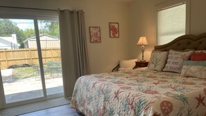 A bedroom with a large bed, a nightstand, a lamp, and a view of the backyard through a sliding glass door.