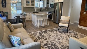 A modern kitchen with white cabinetry, a stainless steel refrigerator, and a dining area with a white table and chairs.