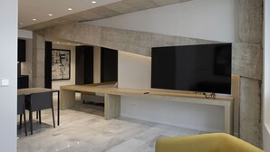 A modern living room with a large flat-screen TV mounted on a concrete beam, a wooden coffee table, and a yellow armchair. - Mon Suites Fetén (Valencia)