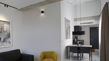 Een moderne woonkamer met een bank, een gele fauteuil, een eettafel met stoelen en een keuken in de achtergrond.