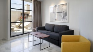 A modern living room with a grey sofa, a yellow armchair, and a coffee table. There is a large window with a view of a balcony and outdoor furniture. - Mon Suites Fetén (Valencia)