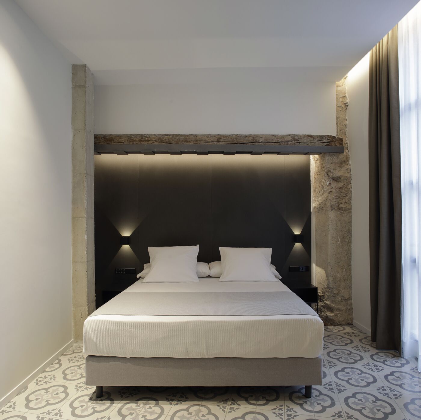 A modern bedroom with a large bed, two bedside lamps, and a stone accent wall.