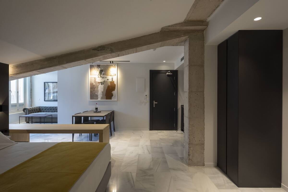 A modern interior with exposed concrete beams, a dining area, a sofa, and a bed.