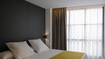 Una habitación de hotel moderna con una cama grande, una pared de acento oscura y un ventanal con cortinas translúcidas.