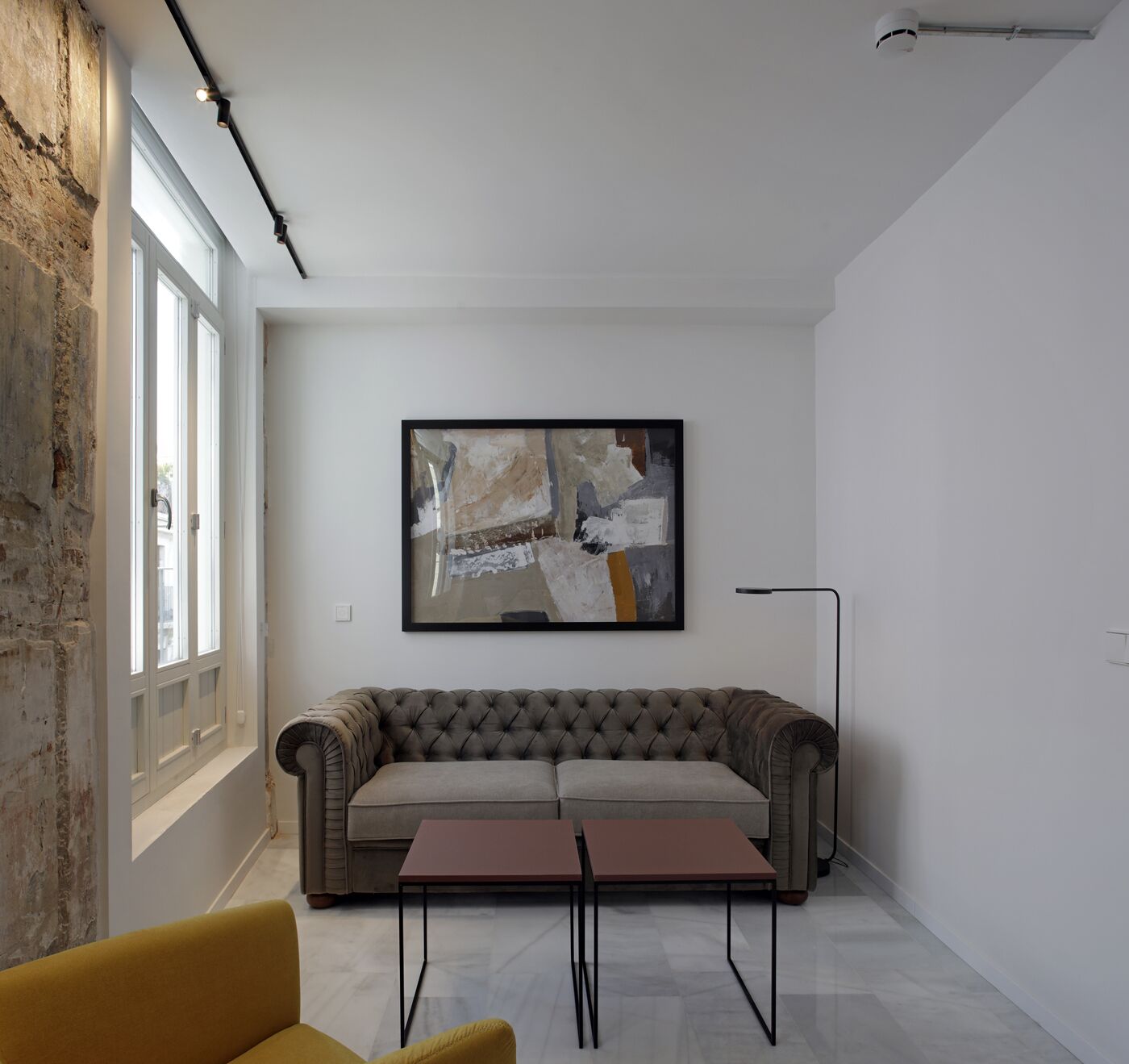 A modern living room with a grey sofa, a small table, and a large abstract painting on the wall.