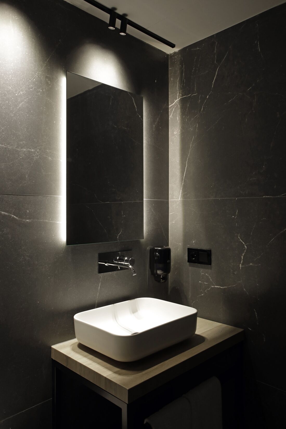 Un baño moderno con un espejo grande, un lavamanos rectangular y un grifo de pared.