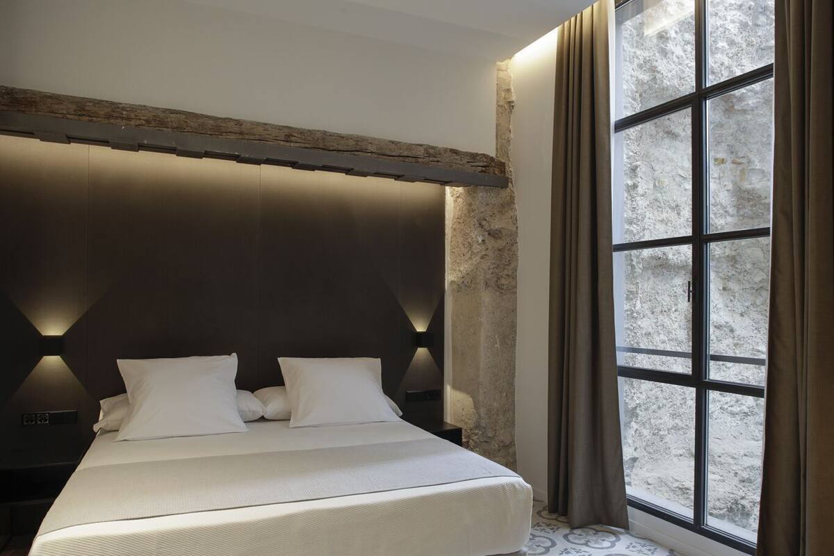 A modern bedroom with a large bed, a stone accent wall, and a large window with curtains.