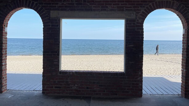 Blick auf einen Strand durch eine Backsteinarchitektur mit Rundbögen.
