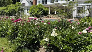 Ein großes Haus mit einer überdachten Veranda und einem Garten voller blühender Blumen.