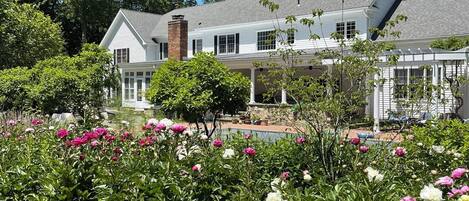 A large house with a covered porch and a garden with blooming flowers.
