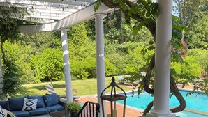 Ein überdachter Patio-Bereich mit Pool, Gartenmöbeln und einer Steinwand.