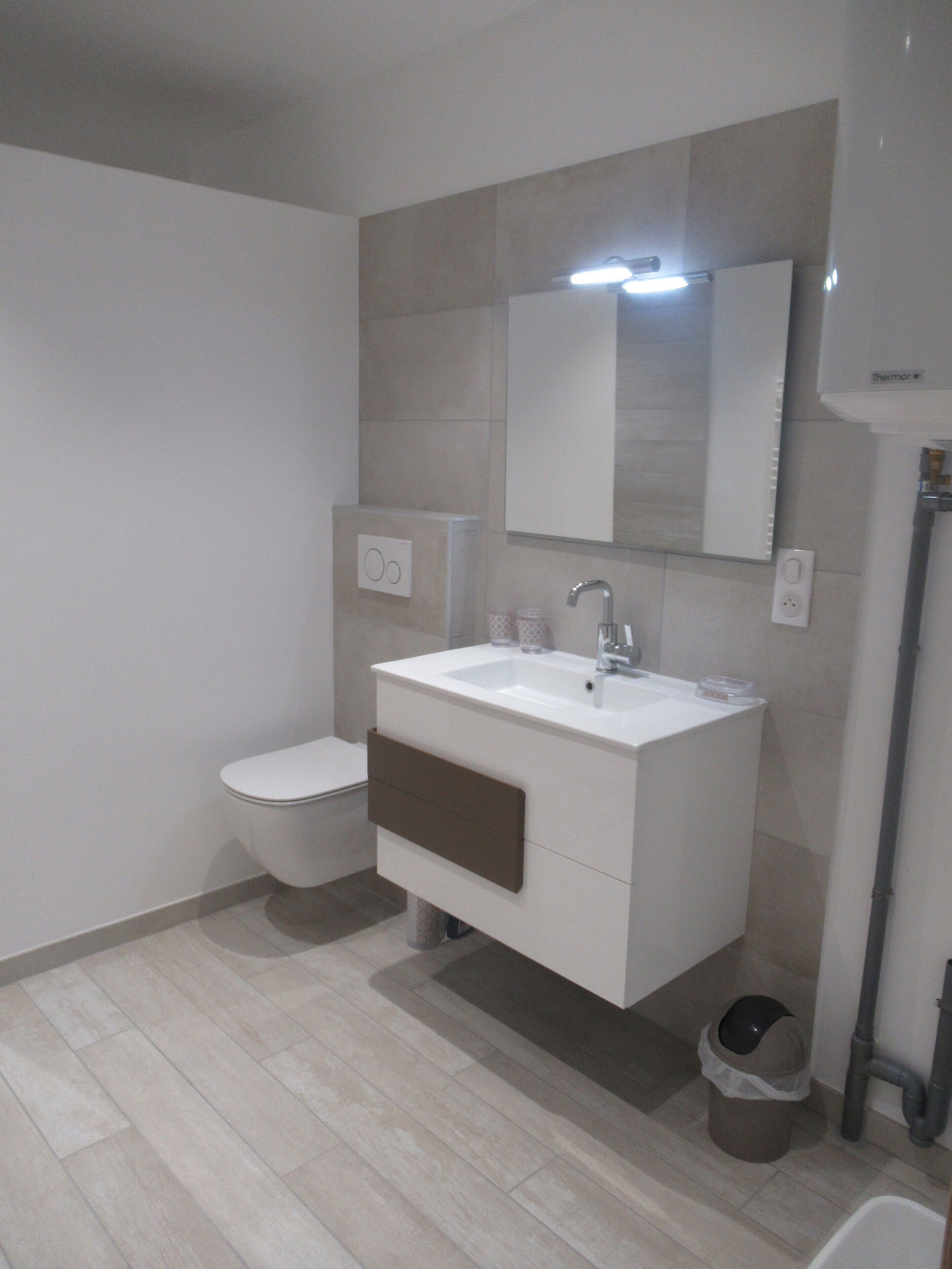 Un baño moderno con un lavamanos blanco, inodoro y espejo.