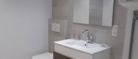Un baño moderno con un lavamanos blanco, inodoro y espejo.