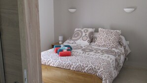Un dormitorio con cama de madera, ropa de cama estampada, una mesita de noche con lámpara y una lámpara colgante.