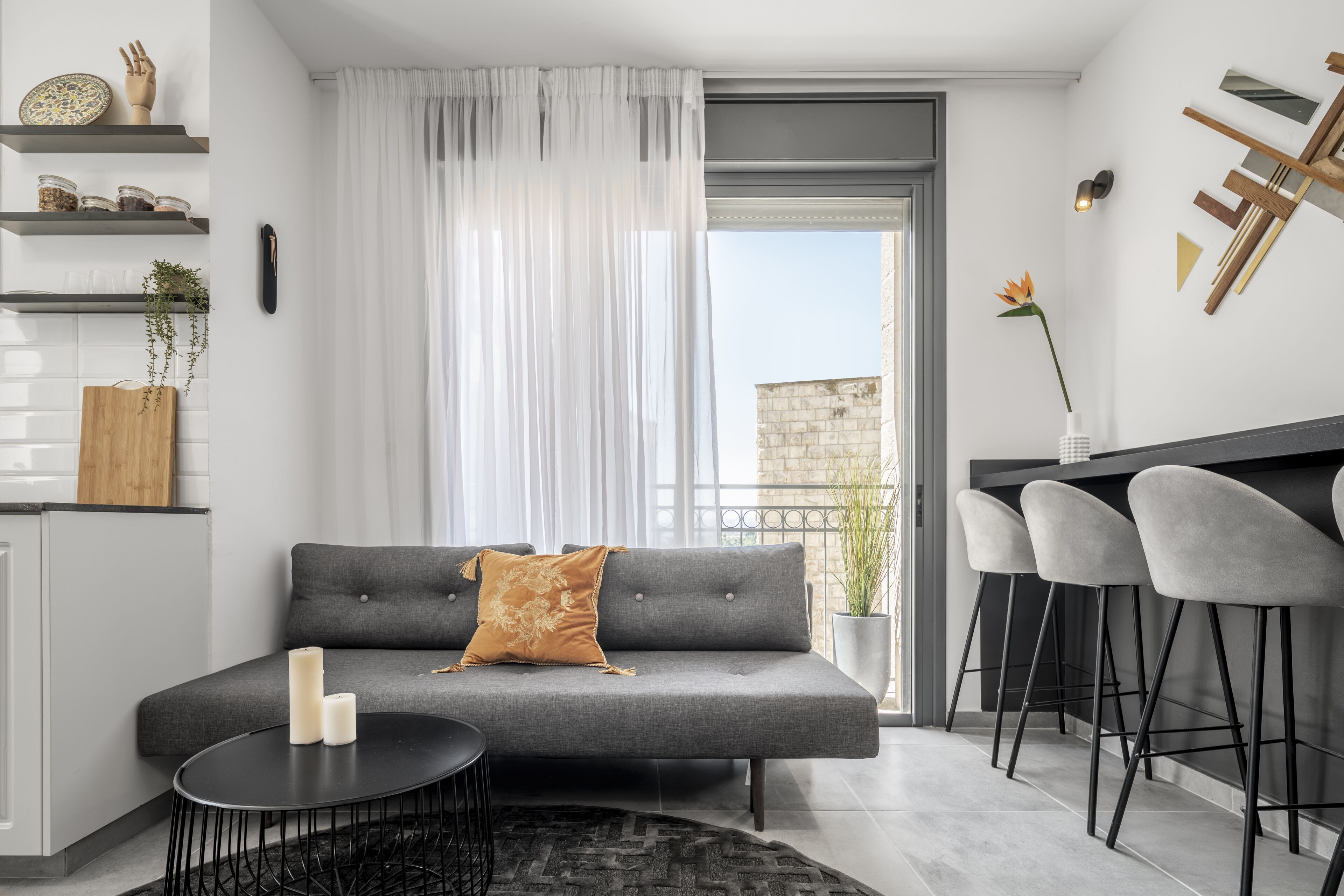 A modern living room with a grey sofa, a small round table, and a bar area with two bar stools.