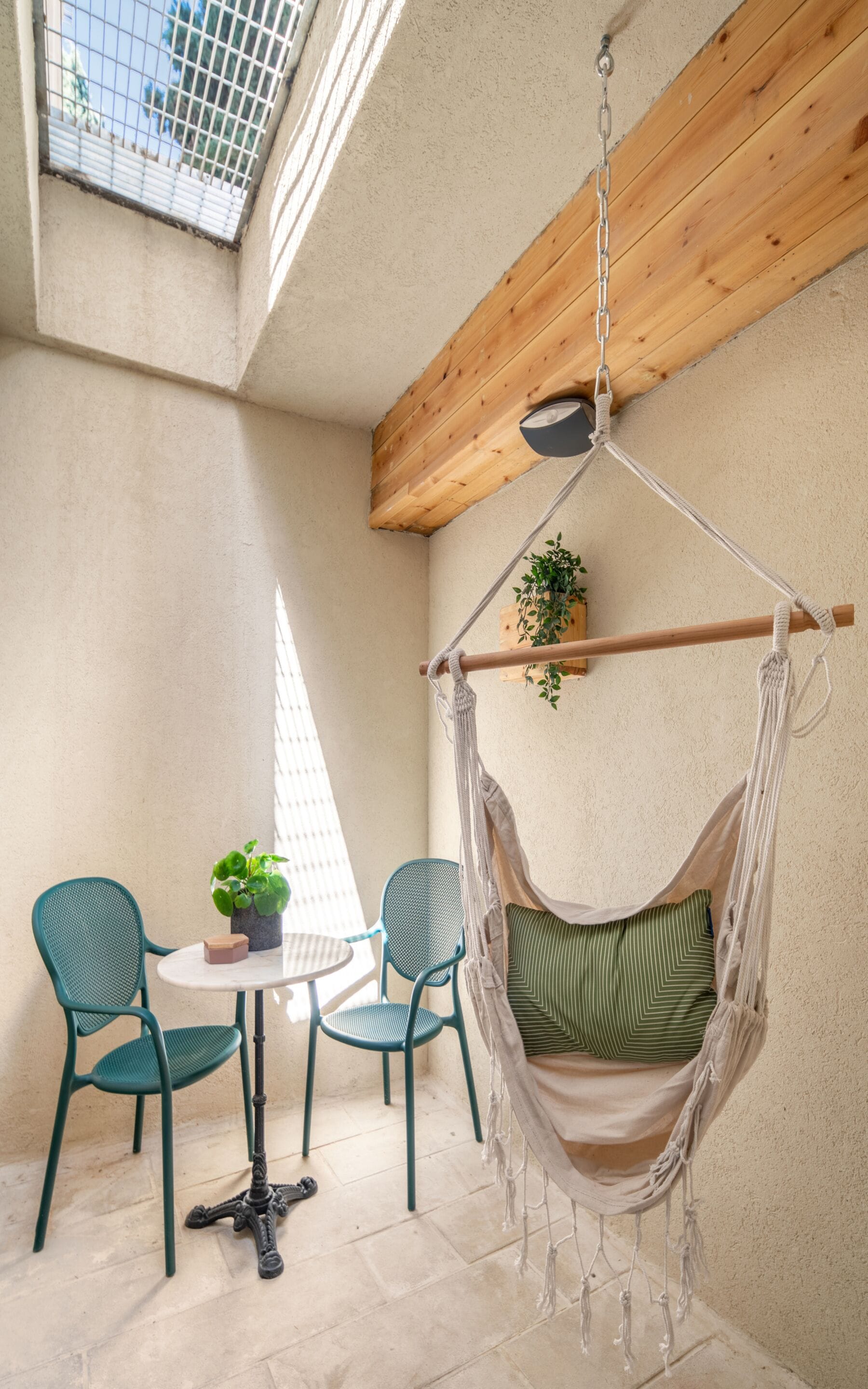 A cozy room with a hammock chair, two chairs, a small table, and a potted plant.