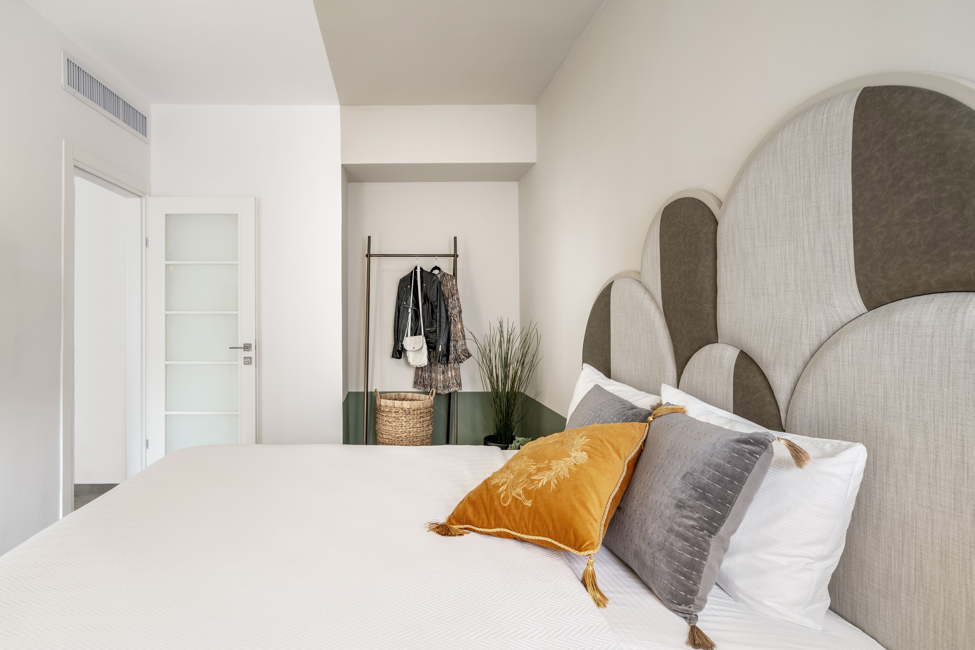 Een slaapkamer met een groot bed, een hoofdbord met een uniek ontwerp, een nachtkastje met een plant en een kledingrek.