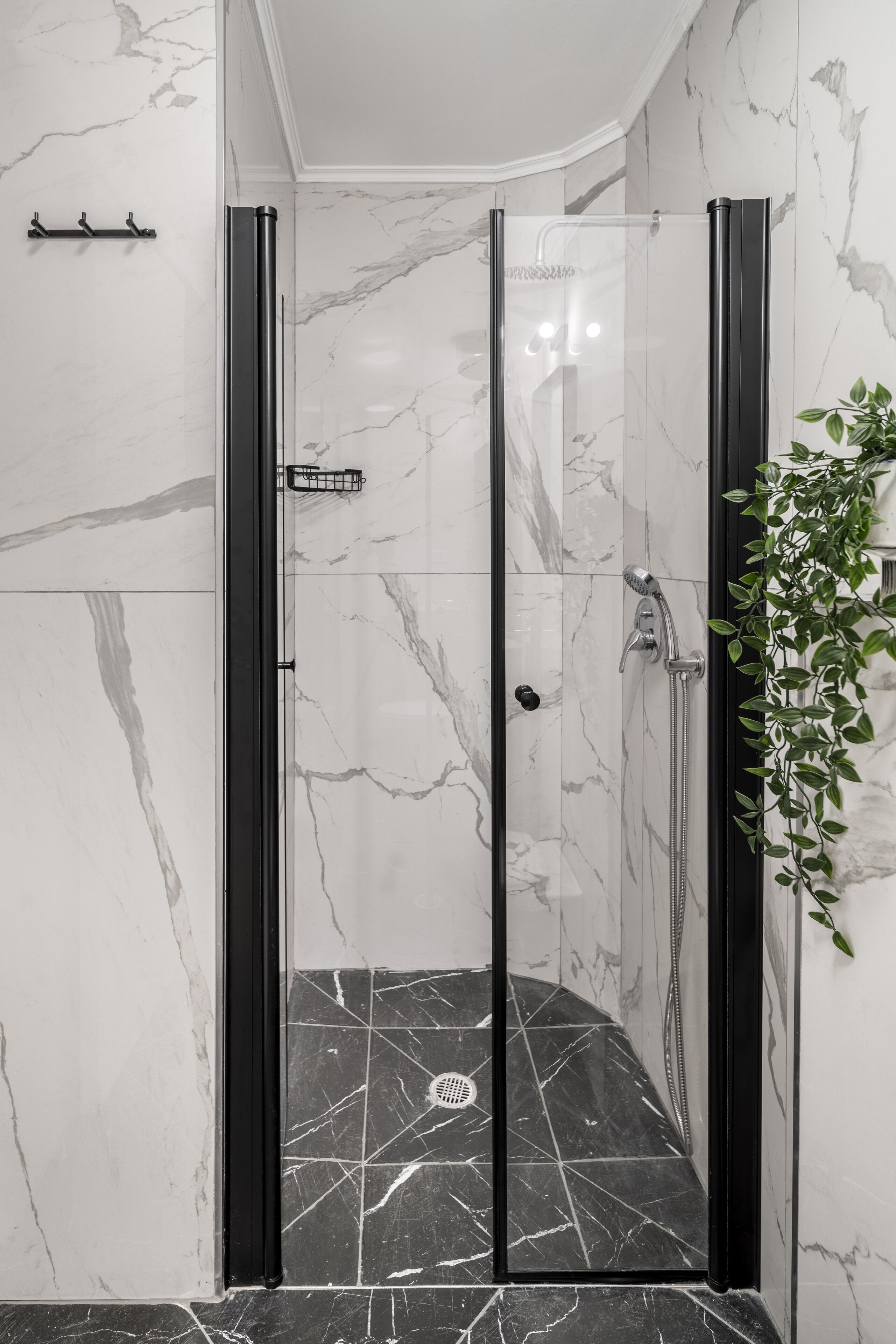 A glass-enclosed shower with a black floor and marble walls.