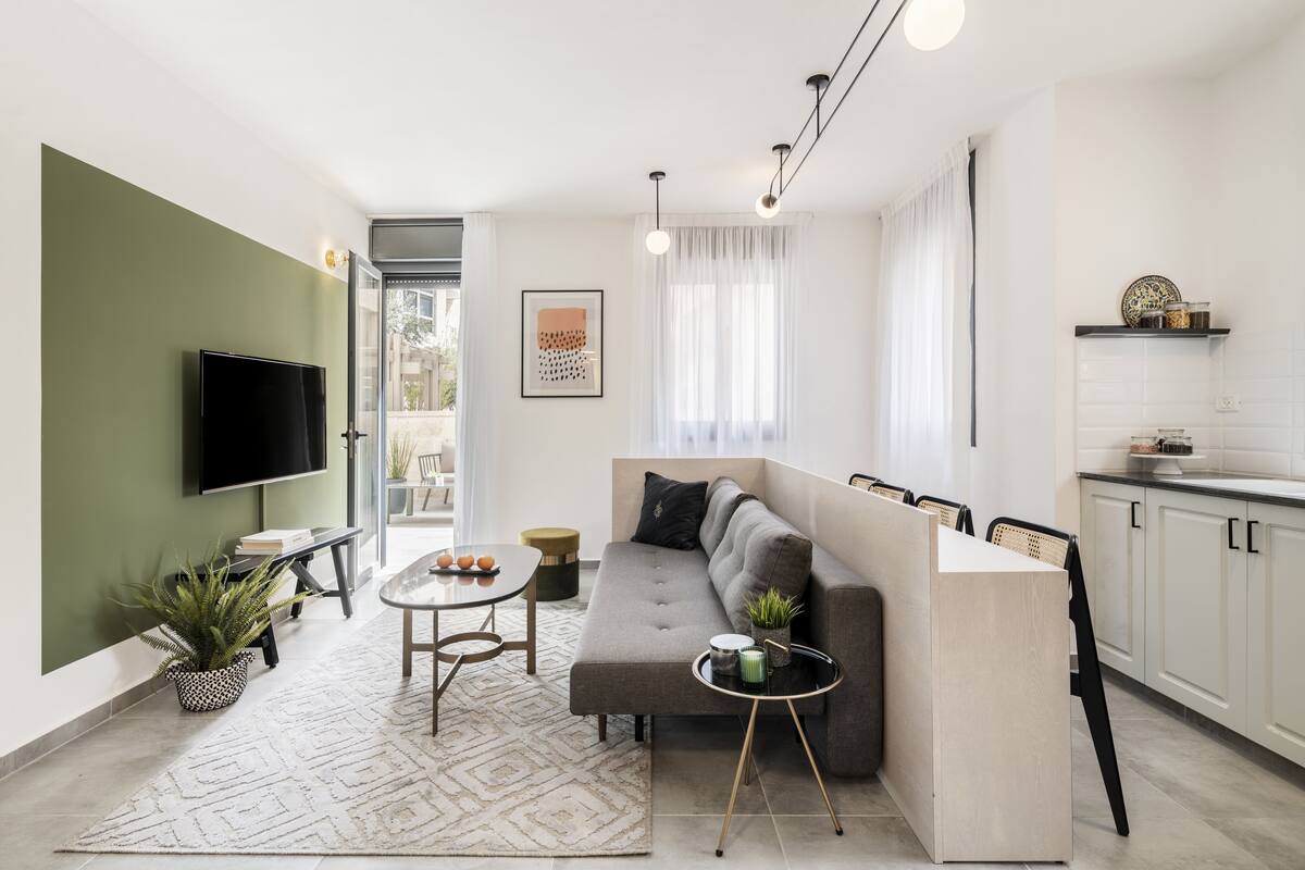 A modern living room with a sofa, a coffee table, a TV, and a kitchen area with cabinets and a countertop.