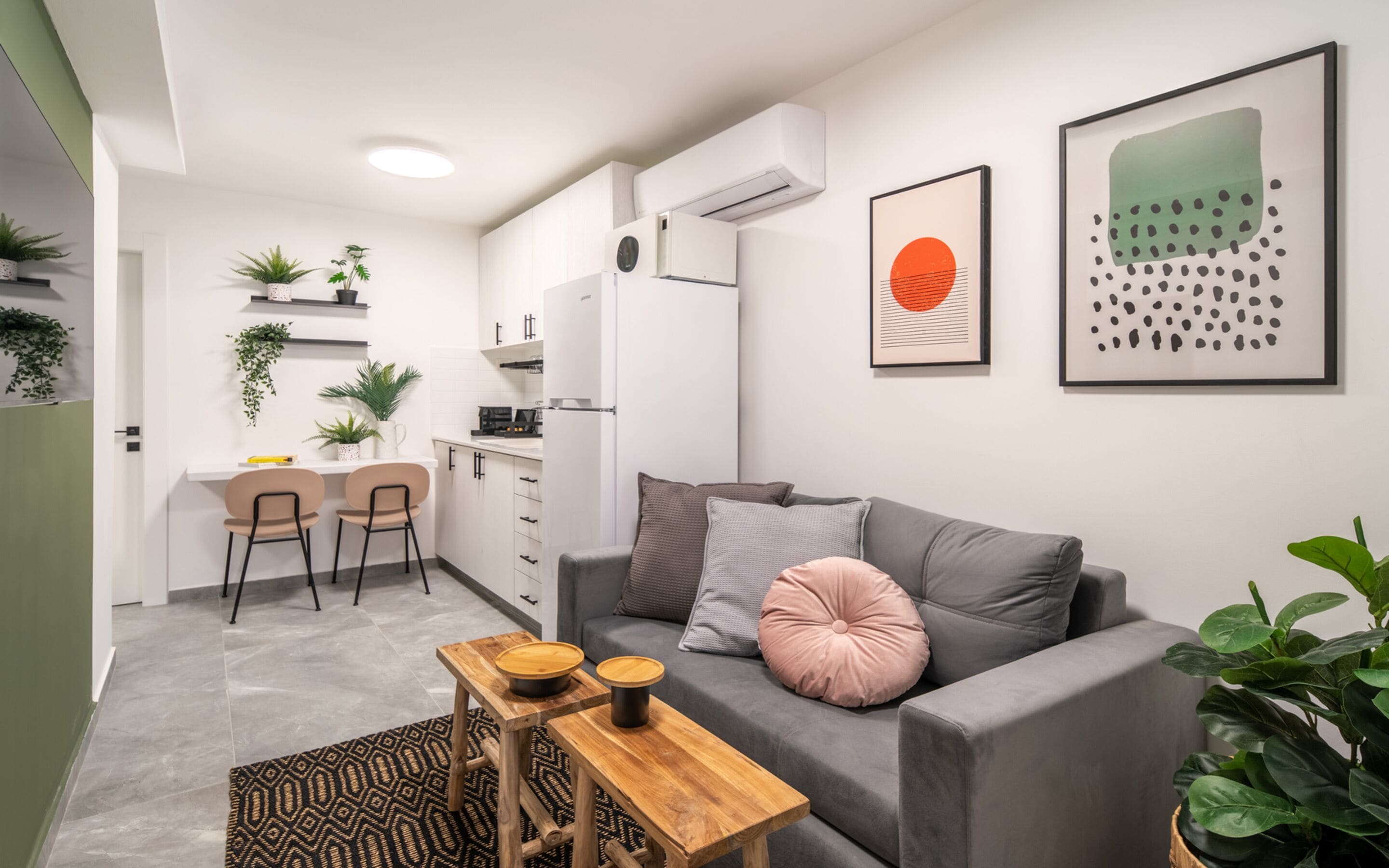 Un salon moderne avec un canapé gris, une table basse en bois et un coin cuisine doté de meubles blancs et d’une cuisinière noire.