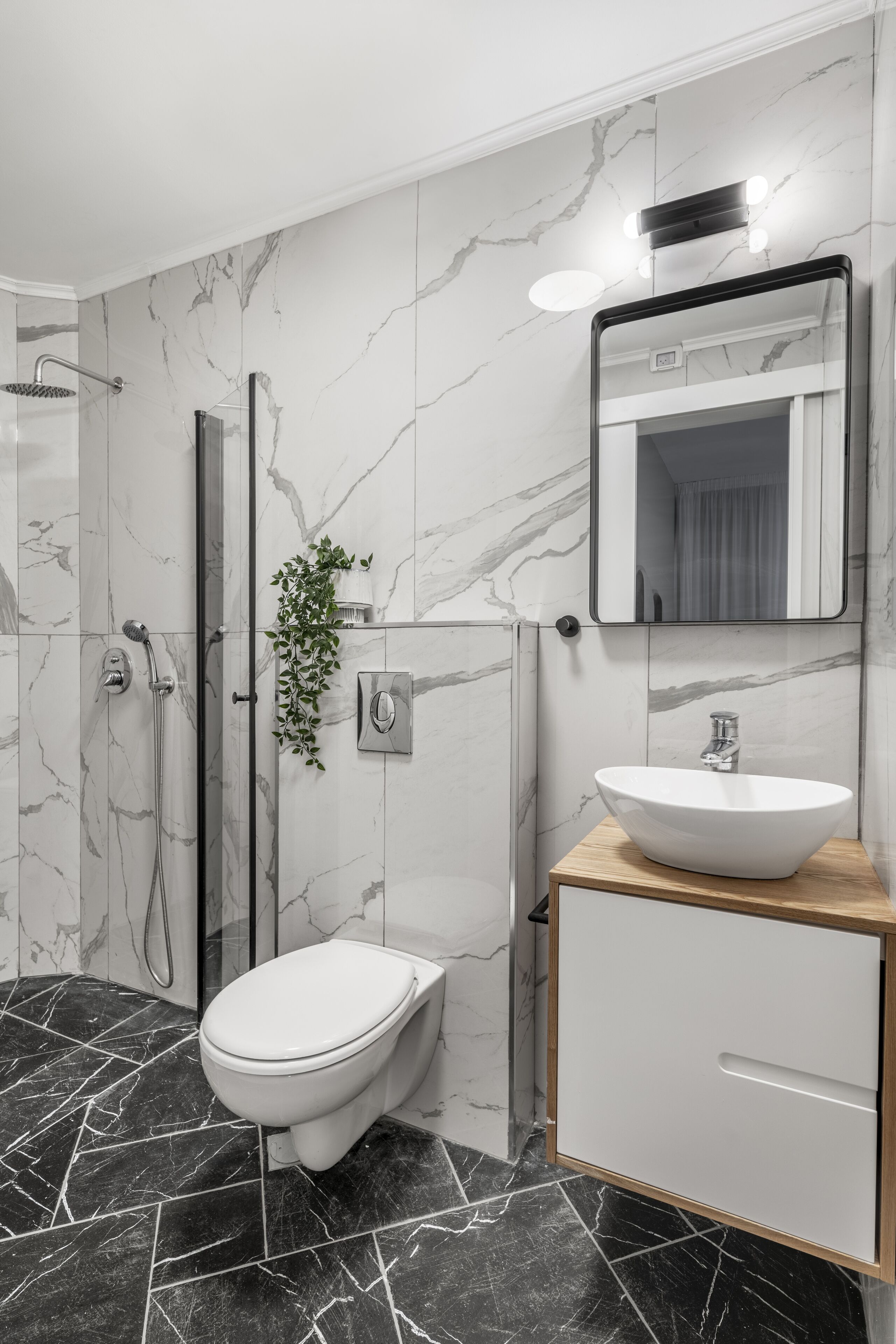 Un baño moderno con inodoro blanco, lavamanos con encimera de madera, espejo con iluminación y ducha con puerta de cristal.