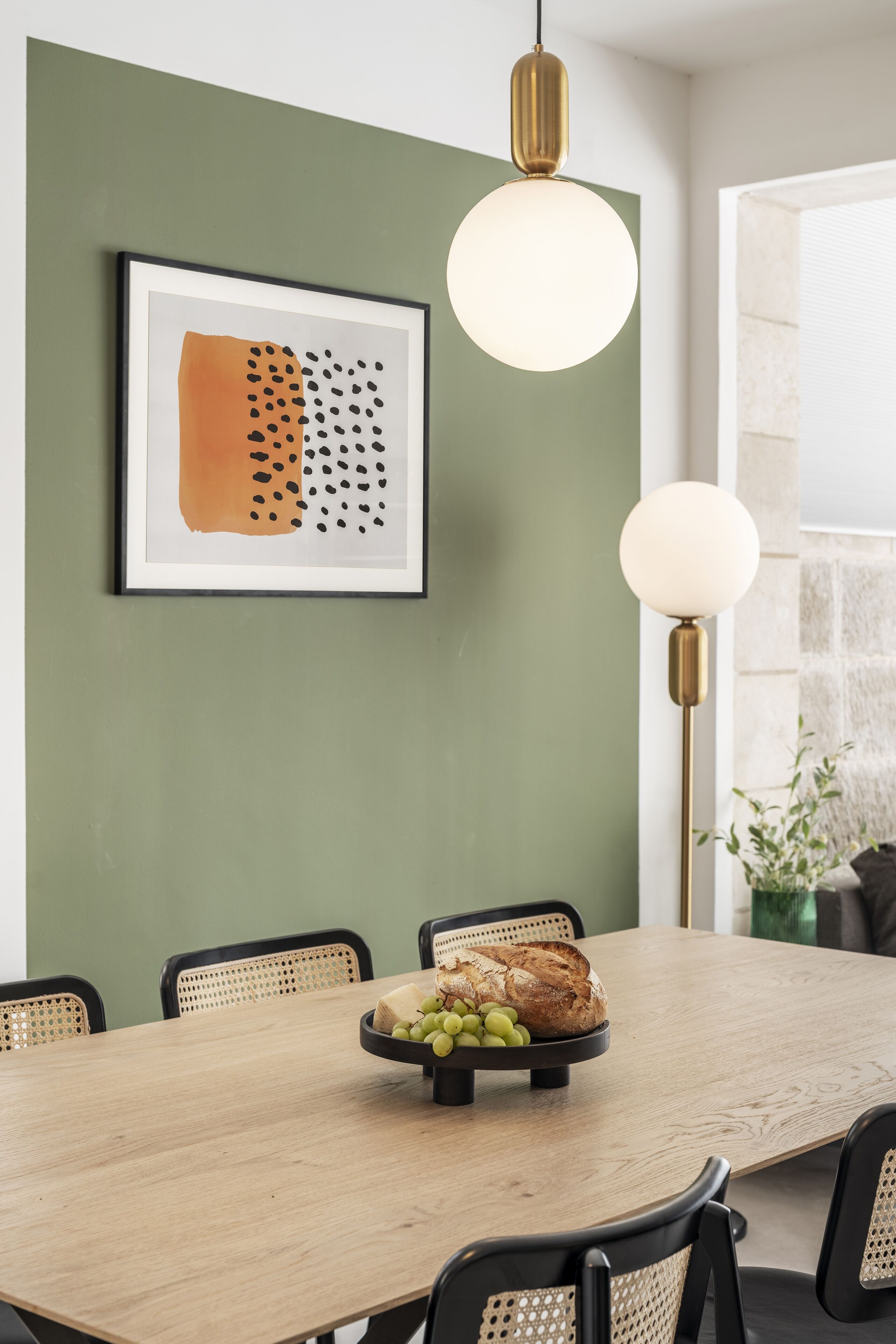 Un'area pranzo con un tavolo in legno, sedie nere, un'opera d'arte astratta incorniciata e una lampada da terra.