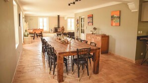 Un vaste espace dédié à la salle à manger, avec une longue table en bois et des chaises, une cuisine en arrière-plan et des œuvres d’art accrochées aux murs.
