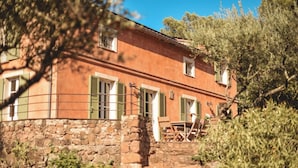 Un bâtiment rustique, avec des fondations en pierre, des volets verts, et une table et des chaises en bois disposées au premier plan.