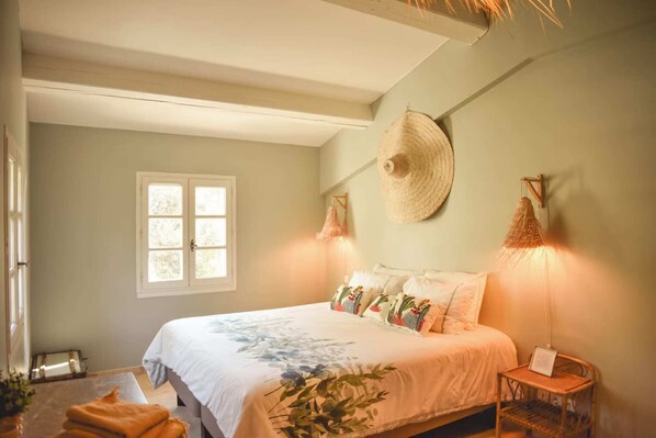 Un dormitorio con una cama, una ventana, un sombrero colgado en la pared y una mesita de noche con una lámpara.