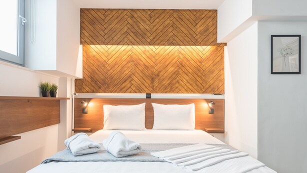 Moderni hotellihuone, jossa on kalanruotokuvioitu puupanelointi katossa, puinen pääty ja suuri sänky, jossa on valkoiset lakanat ja sininen torkkupeitto.