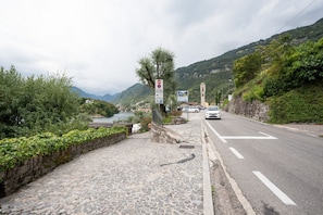 A paved road with a stone pathway, a vehicle, and a view of a lake and mountains in the distance.