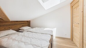 Una camera da letto con soffitto spiovente, testiera in legno, due letti con biancheria bianca e un lucernario.