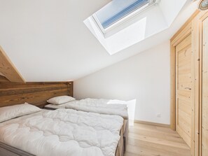 A bedroom with a sloped ceiling, wooden headboard, two beds with white bedding, and a skylight. - Superb central duplex with spa access, terrace, and parking (Les Gets)