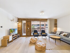 A modern living room with a sofa, two armchairs, a coffee table, a TV, and a wooden floor. - Superb central duplex with spa access, terrace, and parking (Les Gets)
