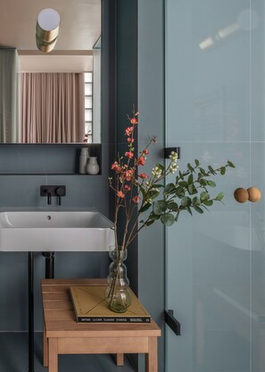 Uma casa de banho moderna com uma sanita branca, um espelho e um vaso com flores sobre uma pequena mesa de madeira.