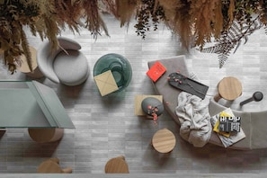A modern living room with a grey brick wall, round wooden tables, a glass coffee table, and a sofa with books and a decorative branch. - Buckle Street Studios by Locke, Aldgate (London)