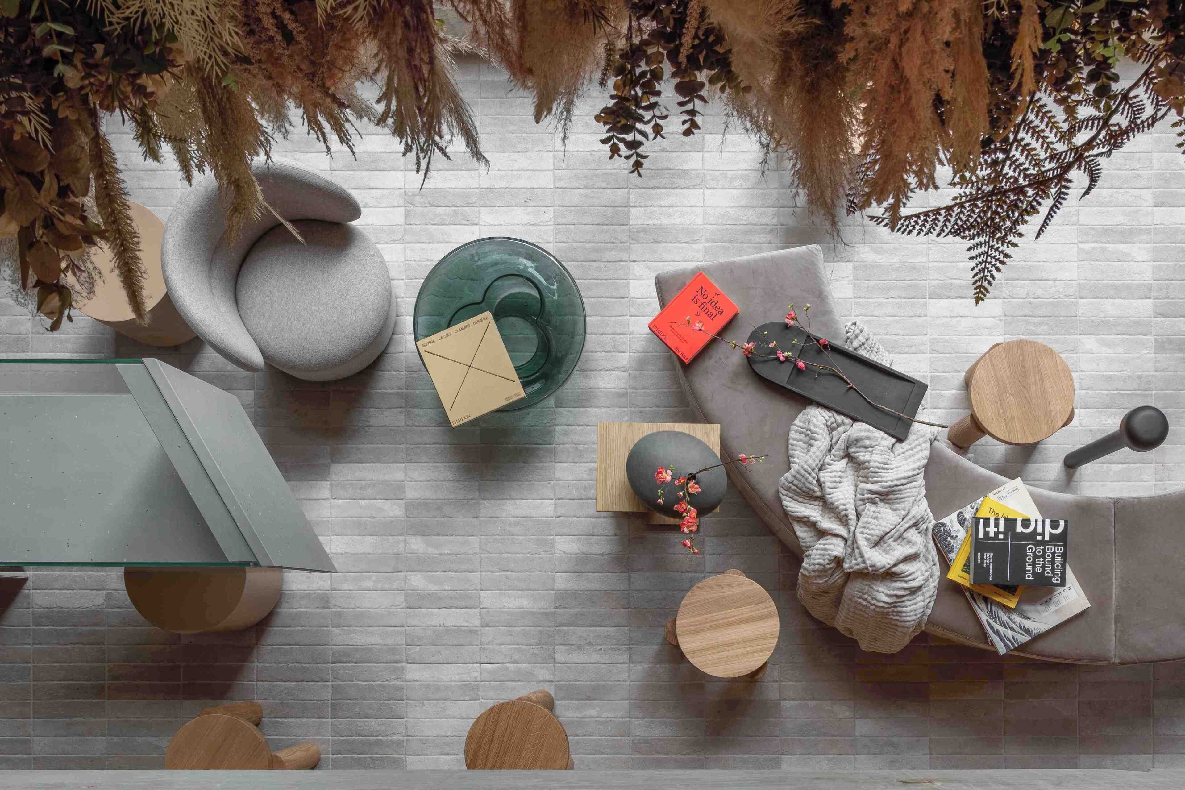 A modern living room with a grey sofa, round wooden tables, a glass coffee table, and a bookshelf.