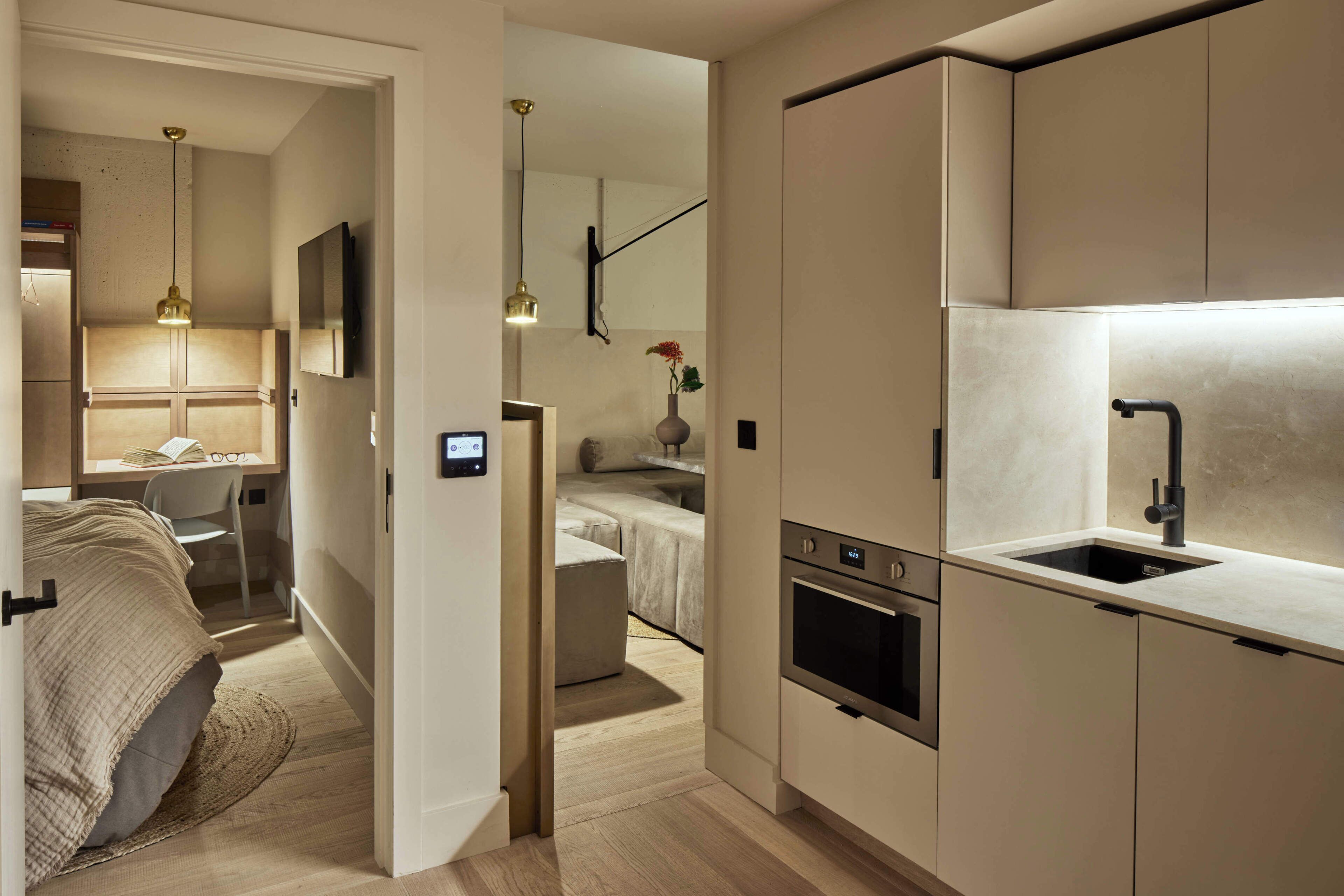 A modern kitchen with built-in appliances, a dining area, and a bedroom with a large bed and reading area.