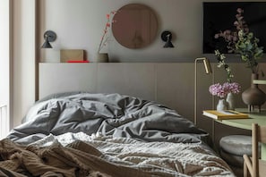 Quarto com cama, mesa de cabeceira, luminária na parede e espelho.