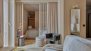 A modern hotel room with a sofa, a small table with a book, a round ottoman, a TV stand, and a bed with a headboard. - Buckle Street Studios by Locke, Aldgate (London)