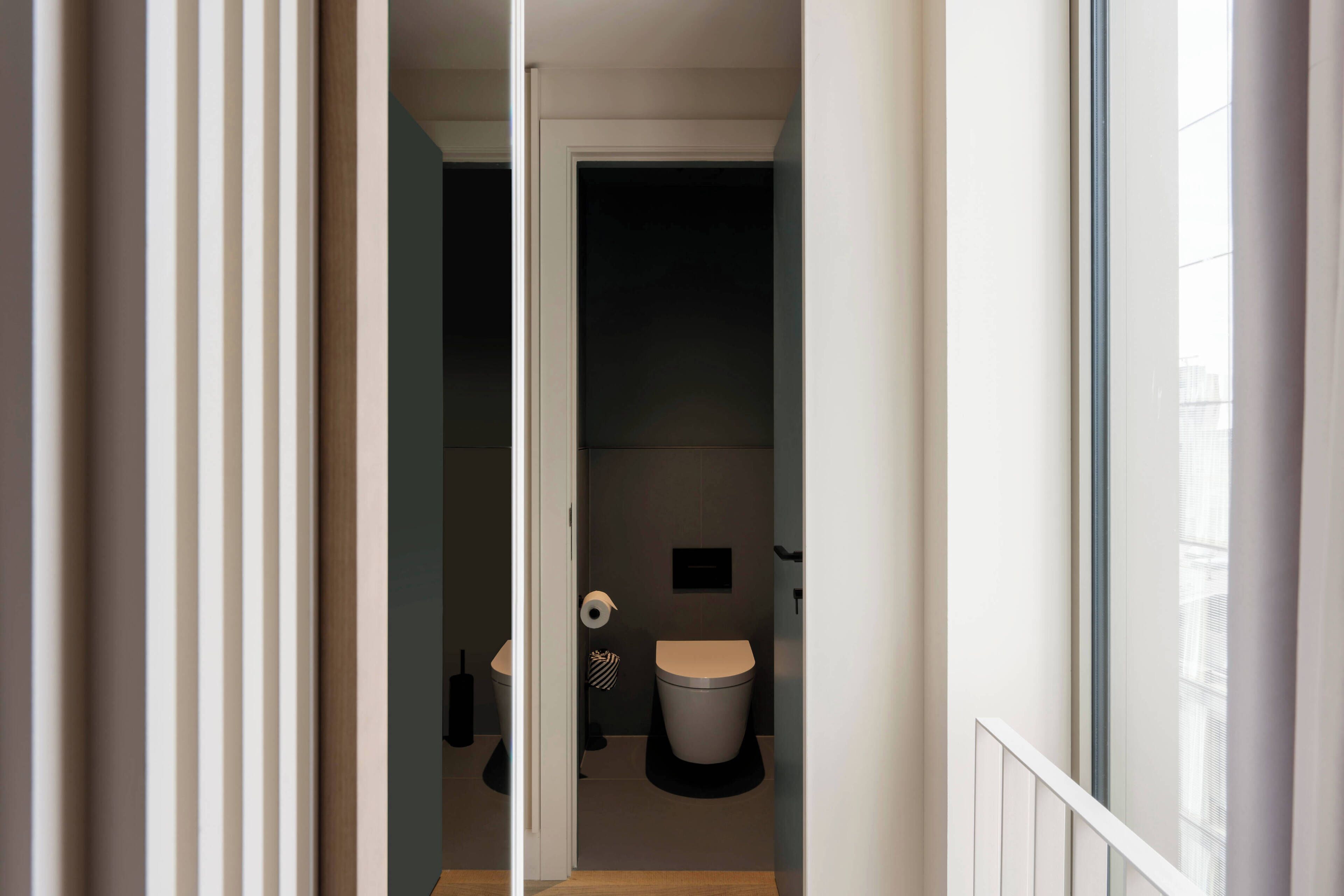A narrow hallway leading to a small, modern bathroom with a toilet, a towel, and a toilet paper holder.