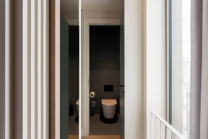 A narrow hallway leading to a small, modern bathroom with a toilet, a towel, and a toilet paper holder.
