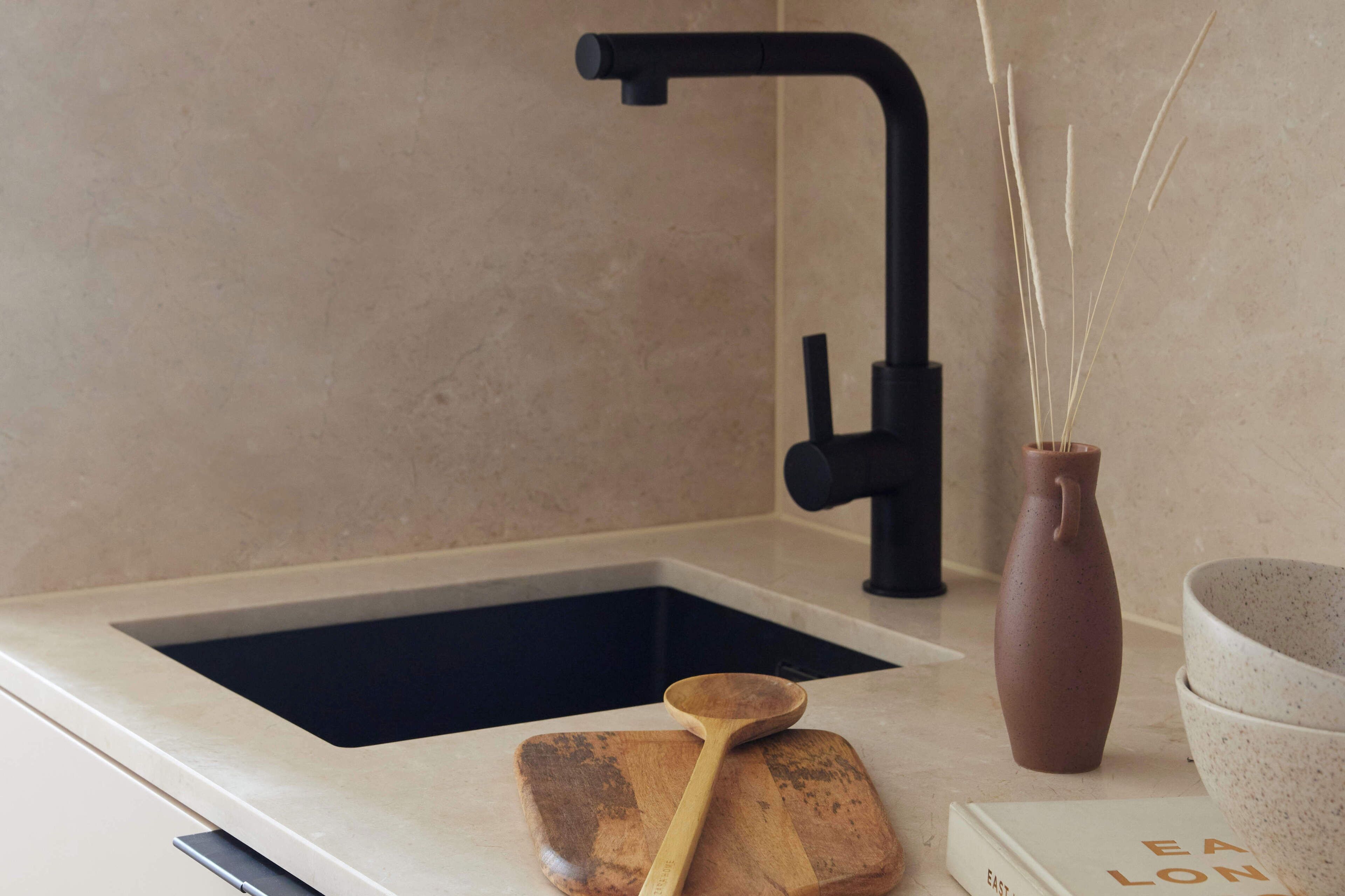 A kitchen with a black faucet, a wooden cutting board, a brown vase, and a bowl.
