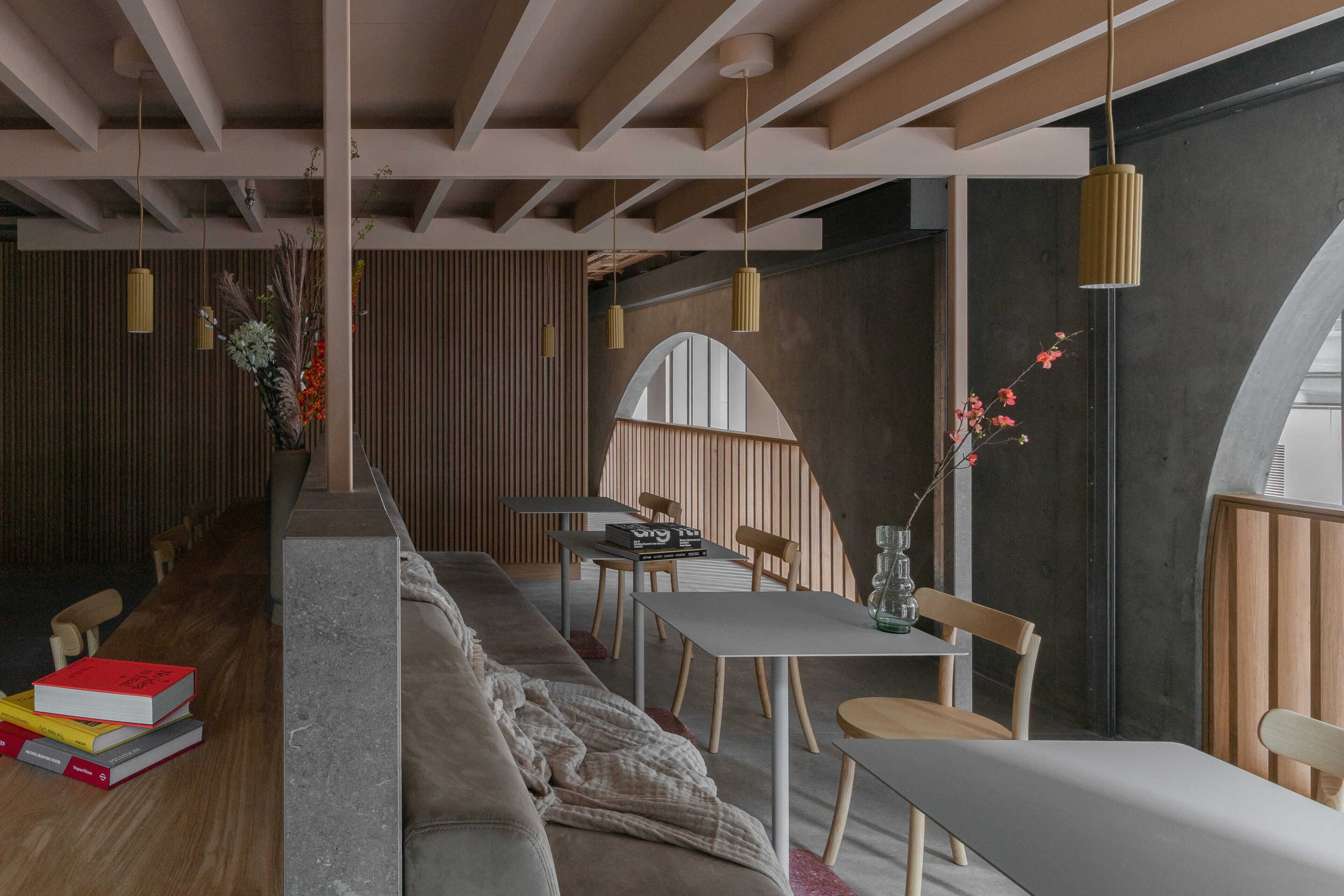 Un intérieur moderne avec un long banc, une table à manger et des chaises, des poutres en bois au plafond et des luminaires suspendus.