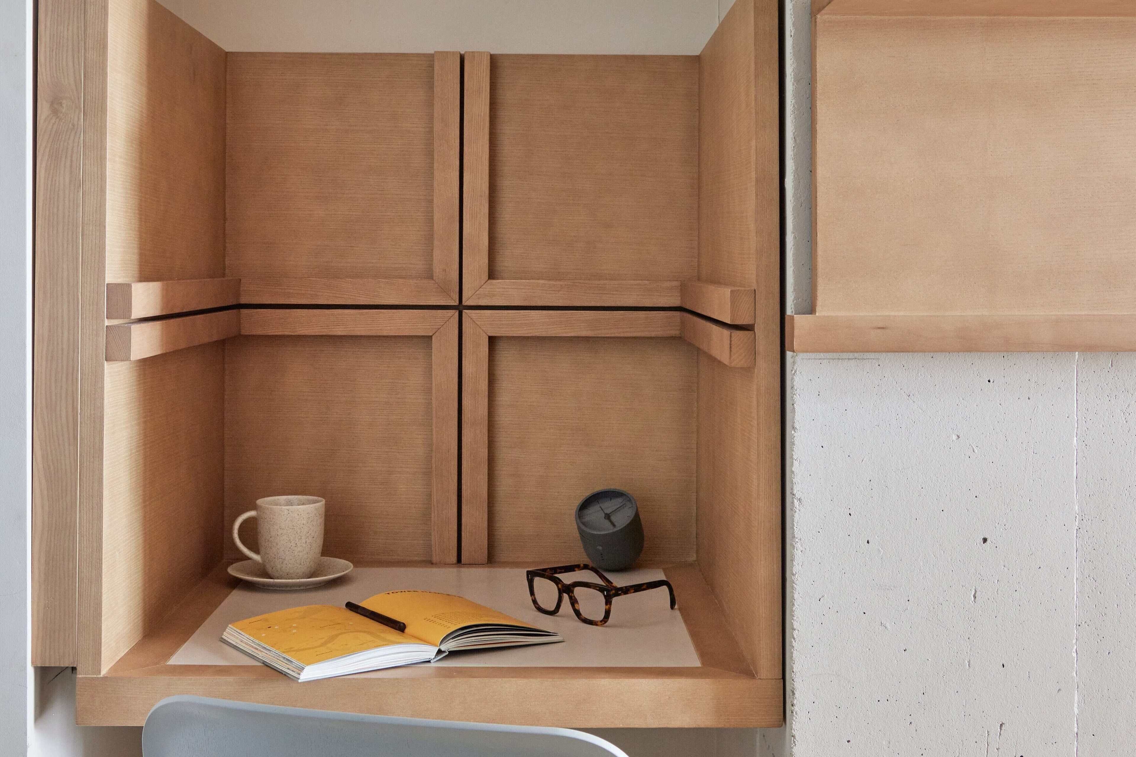 A wooden desk with a cup, glasses, a book, and a clock.