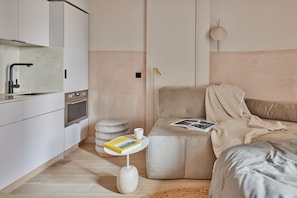 A modern kitchen with a built-in oven and a sink, a cozy seating area with a cushioned bench and a small table, and a neutral color palette. - Buckle Street Studios by Locke, Aldgate (London)