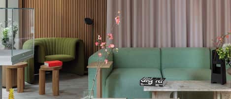 A modern living room with a green sofa, wooden side tables, a glass coffee table, and a hanging light fixture.