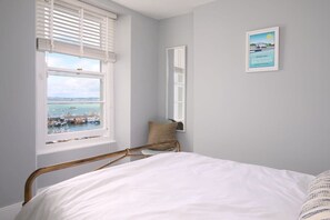 A bedroom with a bed, a window with blinds, a chair, a pillow, and a framed picture on the wall.