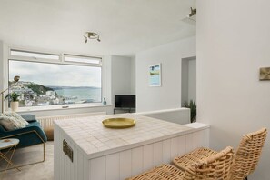 A modern kitchen with a large window, a central island, wicker chairs, and a view of a coastal town.