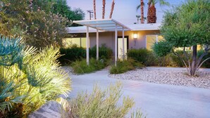 Ein modernes Haus mit überdachter Terrasse, umgeben von verschiedenen Pflanzen und Bäumen.